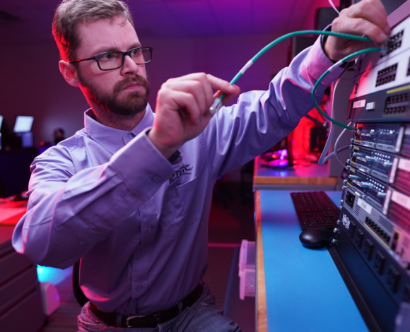 A computer networking technician plugs a wire into a server rack
