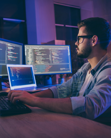 A programmer is lit by the light of many screens as he reviews a software test
