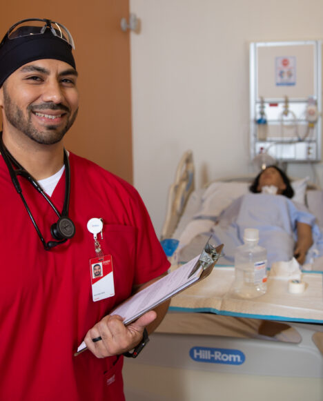 TSTC Nursing student poses wearing red scrubs and a stethoscope while holding a clipboard.