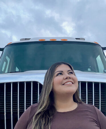 TSTC in Fort Bend's first female CDL student Yesenia Aguinaga stands in front of her 18-wheeler, smiling and looking to the right off-camera.