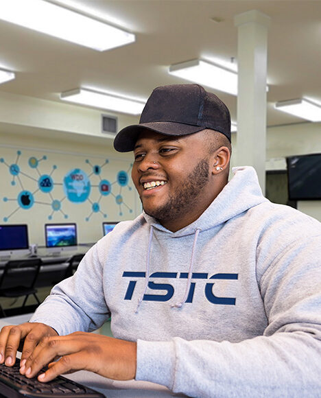 Student in a TSTC hoodie is using a computer and smiling happily.