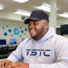 Student in a TSTC hoodie is using a computer and smiling happily.