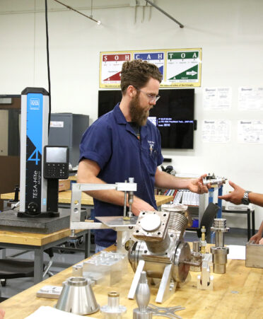 TSTC Precision Machining Technology instructor Taylor Marze, center, hands a sample of a student project to Centerline Manufacturing shop foreman Juan Luna as Centerline CEOs Simon Feinsilver, left, and Tim Rueter, right, learn more about the training pathway during a visit to the lab at TSTC’s campus in Fort Bend County.