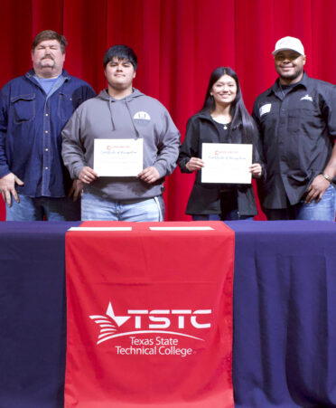 Jerroll Hodge, right, lead instructor of Welding Technology at TSTC’s Fort Bend County campus, presents $11,000 scholarships to Hector Guzman, second from left, and Zitlaly Rangel, second from right, at Cleveland High School. At left is Cleveland High School welding instructor Jim Baxter.