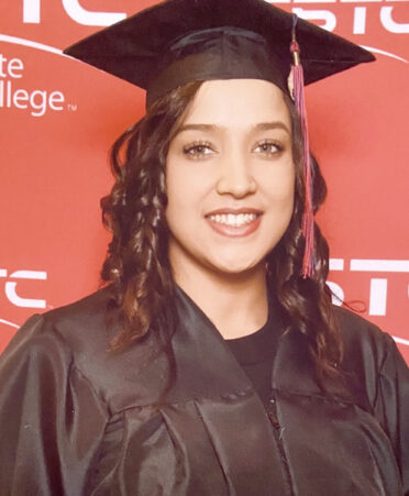 Smiling Brittoni Thornhill poses in front of a red background patterned in TSTC. She wears a black graduation cap and gown.