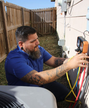 TSTC HVAC alumnus Marco Silva monitors a manifold gauge to ensure that a residential air conditioning system is operating smoothly.