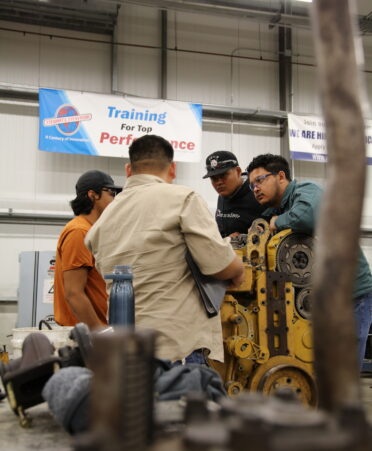 Jose Reyna (second to left) and three students stand around a diesel engine.