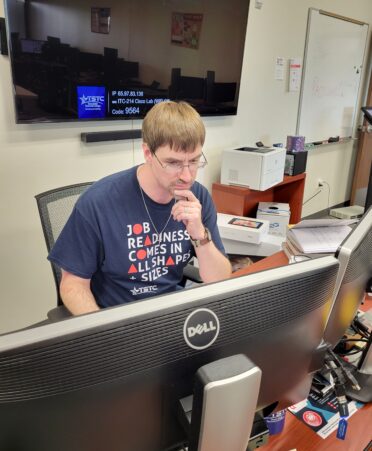 Andrew Phillips sits at his desk looking at the computers in front of him.