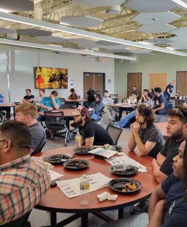 Students sit at tables while a video plays in the background