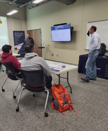 Two students sit and listen to a presentation by two Saber Power representatives on the left and right