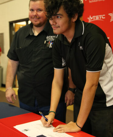 Esequiel Serrano Flores (right), a senior at IDEA Sports Park College Prep in Brownsville, signs his letter of intent to study in the Electrical Lineworker and Management Technology program at TSTC’s Harlingen campus on National CTE Letter of Intent Signing Day.