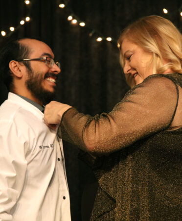 TSTC Dental Hygiene instructor Lucretia Human places a lab coat on William Torres, a graduating TSTC Dental Hygiene student, to recognize him as a dental hygienist during a recent pinning ceremony.