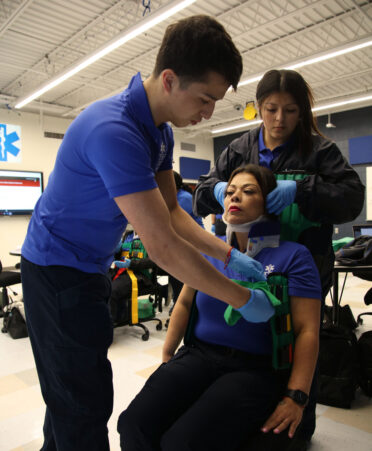 Seth Sanchez (left) practices applying a Kendrick extrication device to his mother, Adriana Sanchez (center), while his sister, Layla Sanchez, assists during a recent lab session at TSTC, where all three are students in the Emergency Medical Services program.