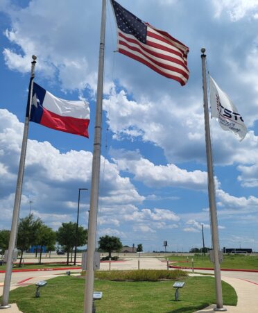 The American flag flies on a flagpole alongside the Texas State flag and TSTC flag.