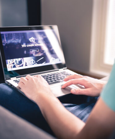 Person wearing light blue shirt sits in recliner and works on laptop