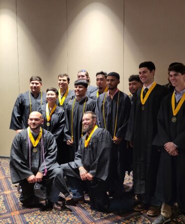 A group of students wearing graduation gowns pose for a camera.