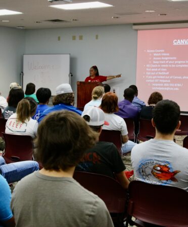 TSTC staff member points to a powerpoint featuring a description of Canvas to a room full of new students