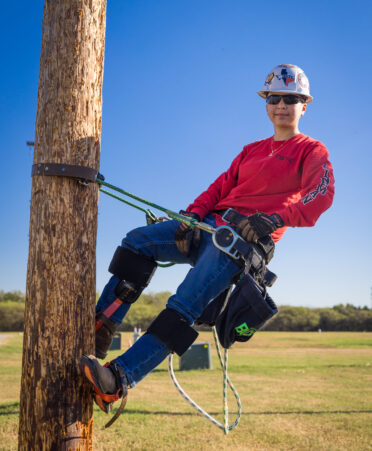 Kelly wearing jeans, a red shirt and safety gear, stands hanging on a harness.