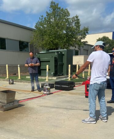Man in white shirt holding a fire extinguisher sprays down a metal container. Three people look on.
