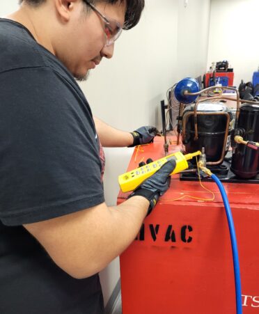 A student wearing a black shirt looks at a yellow device hooked up to a red refrigeration unit.