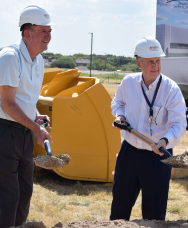 two men in hard hats holding a shovel