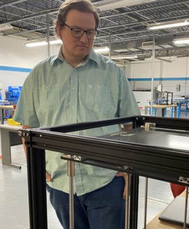 Man in green shirt looking at 3D printer