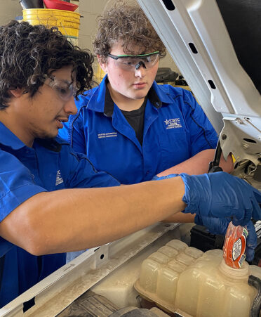 two men in blue shirts checking engine fluid