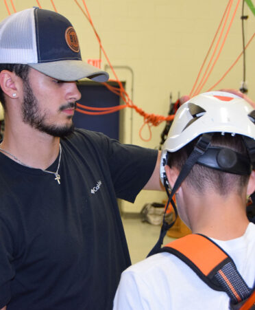 Man with beard wearing a hat helping student with helmet