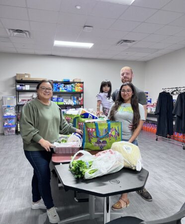 Three people and a child stand over the meal kits resting on a table.