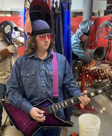 Mn holding guitar wearing a welding hood