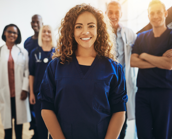 Girl in scrubs smiling while a team of doctors stands behind her smiling.