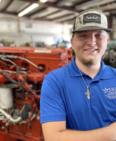 man in blue shirt standing in front of truck engines