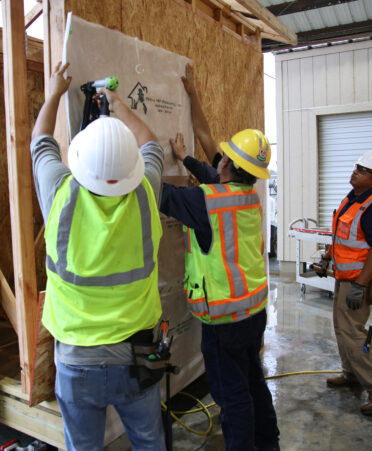 John Robledo (left), a TSTC Building Construction Technology student, and Rene Rodriguez (center), a Building Construction Technology instructor, place a house wrap on a shed to prevent water from damaging the wood, while Luis Trevino, another student in the program, observes their work during a recent lab session.