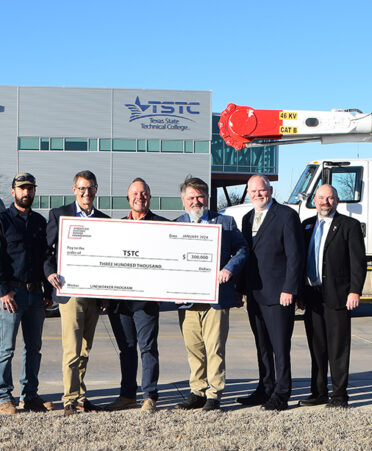 seven men standing in front of trucks holding large check