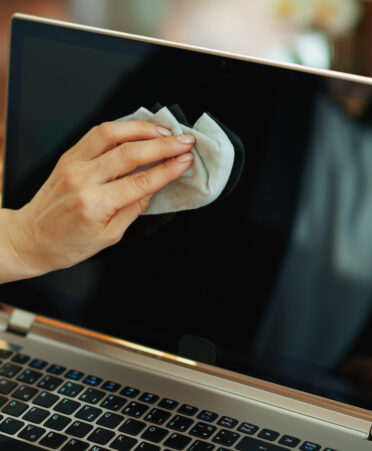 Women's hand wipes off the screen of a laptop with a blue rag