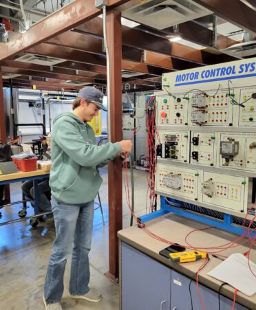 A student wearing jeans and a teal sweatshirt works with wires.