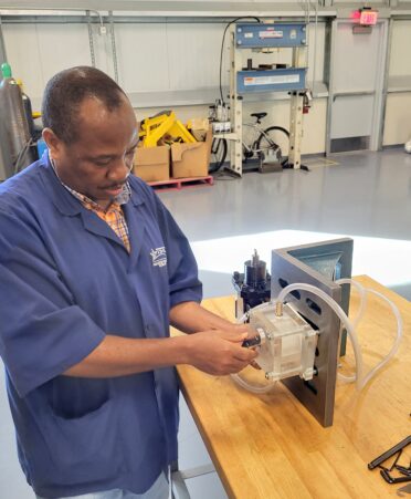 Nizigiyimana, wearing a blue tstc shirt, tinkers with a pump on a table