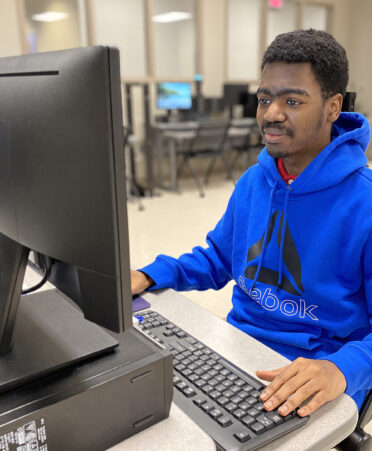 man in blue shirt sitting at computer