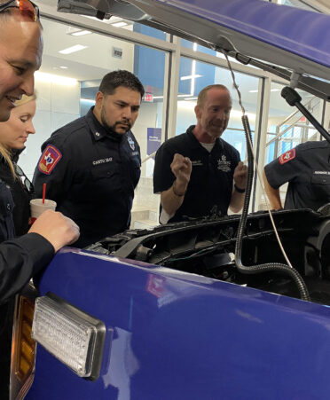 group of people looking under a hood of a vehicle