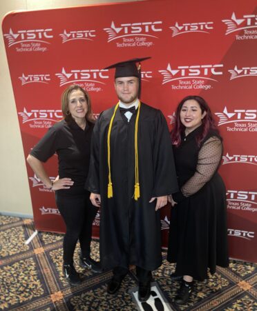 Jessica stands with another program lead and a graduate with a red TSTC backdrop. All are wearing black.