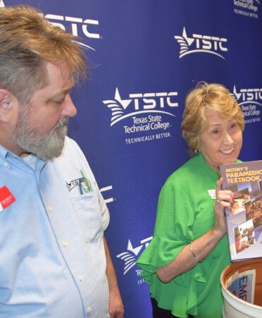 Woman in green shirt holding book while man looks at it