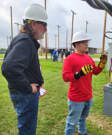 Ron Jones wears a blue sweater and a white hardhat while looking at a student wearing a red shirt and white hard hat