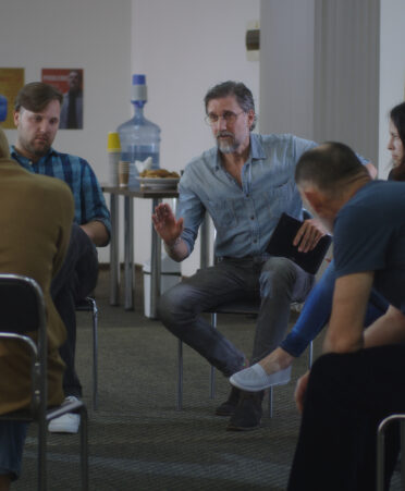 Middle aged bearded man talking and supporting desperate people during support group meeting