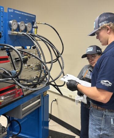 Two students stand at a hydraulics simulator.