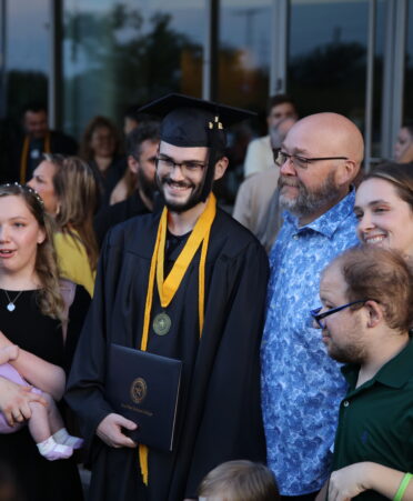 A graduate stands in cap and gown surrounded by his family. All are posing for a picture