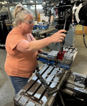 Female student wearing safety glasses pulling on lever to lower a drill of a precision machining mill.