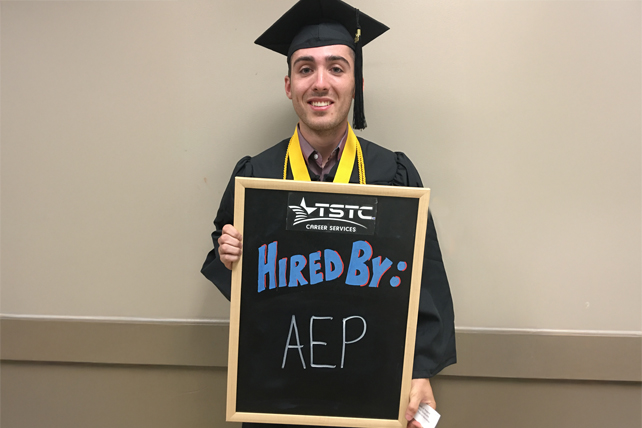 TSTC graduate posing in cap & gown holding a chalkboard showcasing their new employer.