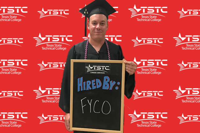 TSTC graduate posing in cap & gown holding a chalkboard showcasing their new employer.
