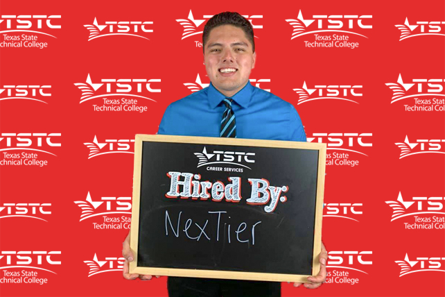 TSTC graduate posing in cap & gown holding a chalkboard showcasing their new employer.