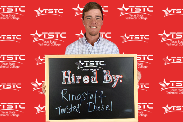TSTC graduate posing in cap & gown holding a chalkboard showcasing their new employer.